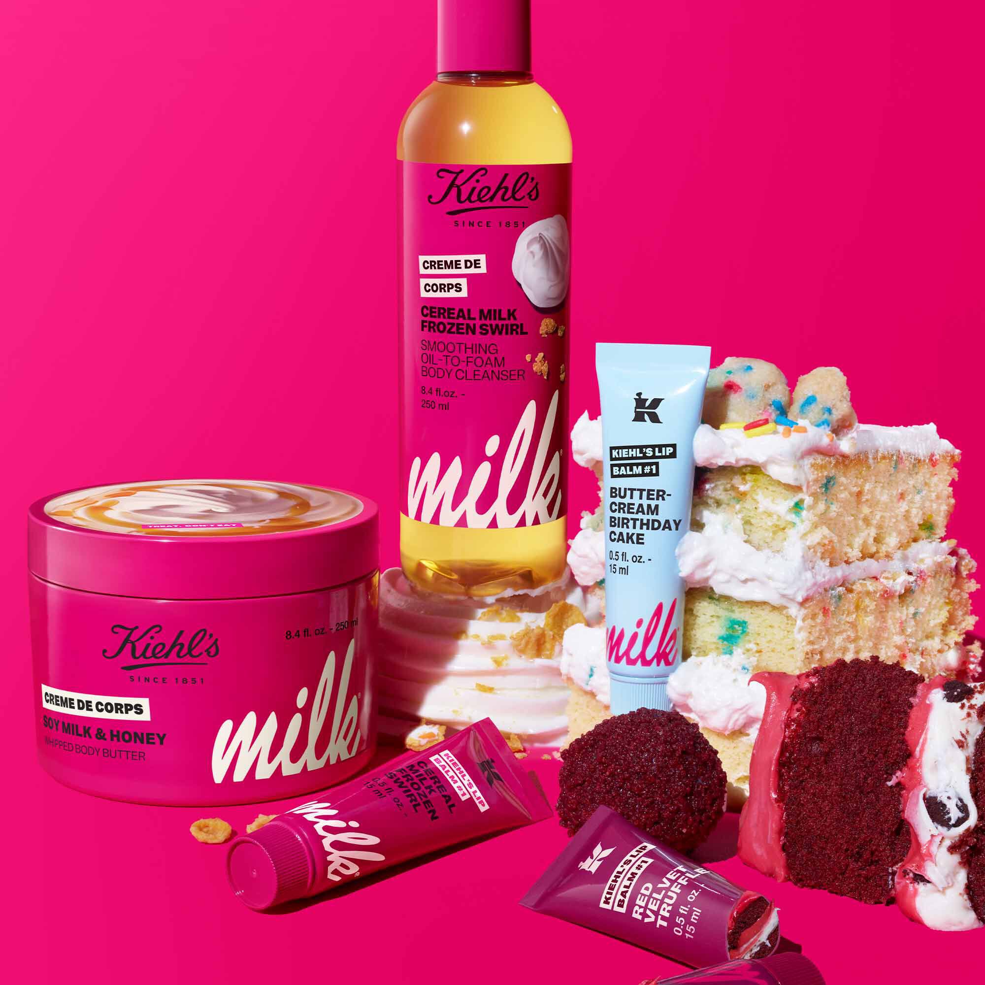 Kiehl’s limited-edition skincare set in pink packaging, featuring mask, cleanser, lip balm, hand cream, and UV serum beside layered cake slices on a bright pink promotional background.​