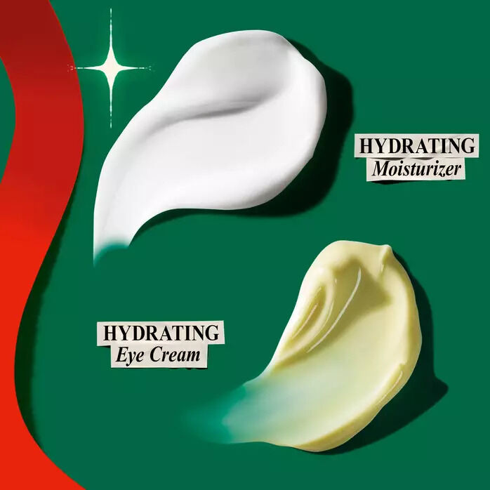 Two cream swatches on a dark green background with a red holiday ribbon: a thick white swatch labeled "Hydrating Moisturizer" and a yellowish swatch labeled "Hydrating Eye Cream."
