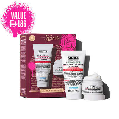 A graphic displaying a white "KIEHL'S ULTRA FACIAL BARRIER-HYDRATING CLEANSER" tube labeled "FULL SIZE" and a smaller white "KIEHL'S ULTRA FACIAL CREAM" jar labeled "TRAVEL SIZE". In the upper right, a pink splattered text box reads "VALUE $40". A partial Kiehl's gift box with a pink graphic bow is visible in the bottom right corner.