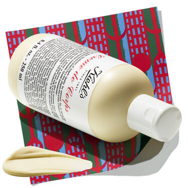 Bottle of Kiehl's Creme de Corps body lotion with a dollop of cream, resting on a patterned holiday background.​